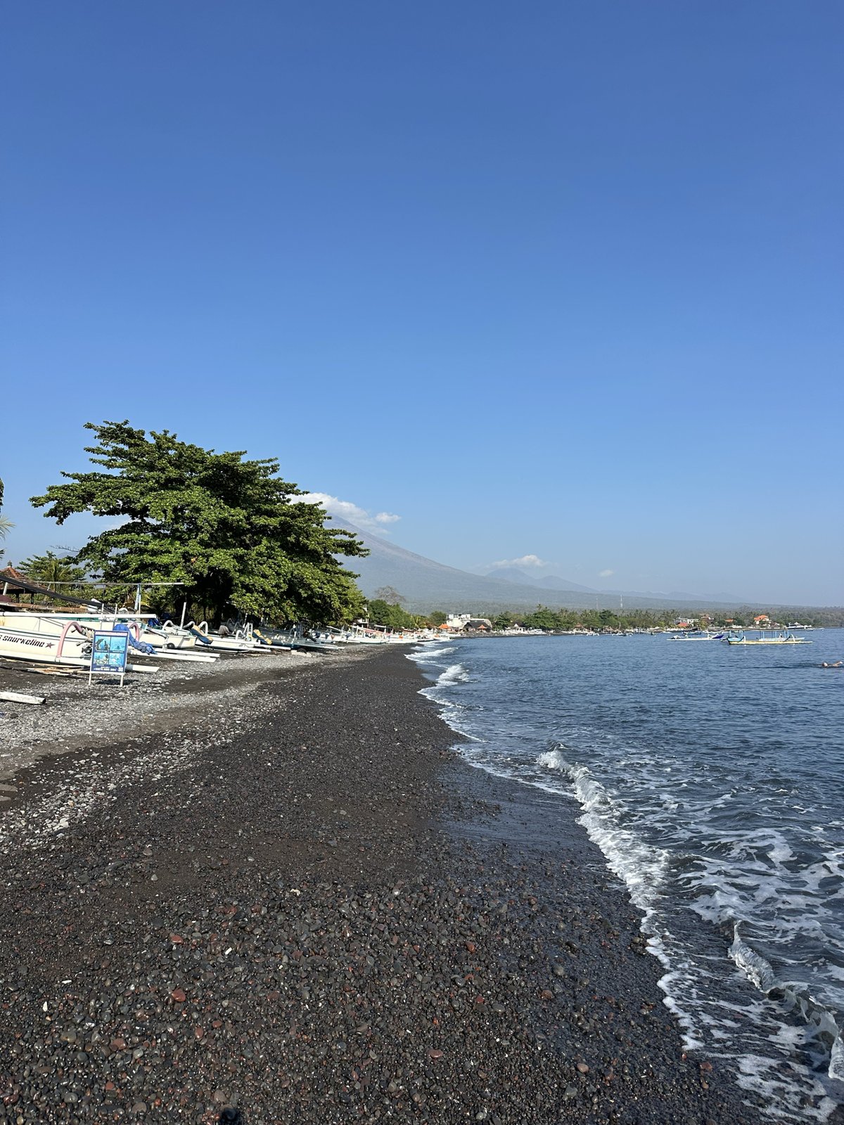 Plage de galets noirs d'Amed avec des jukungs et le Mont Agung au fond