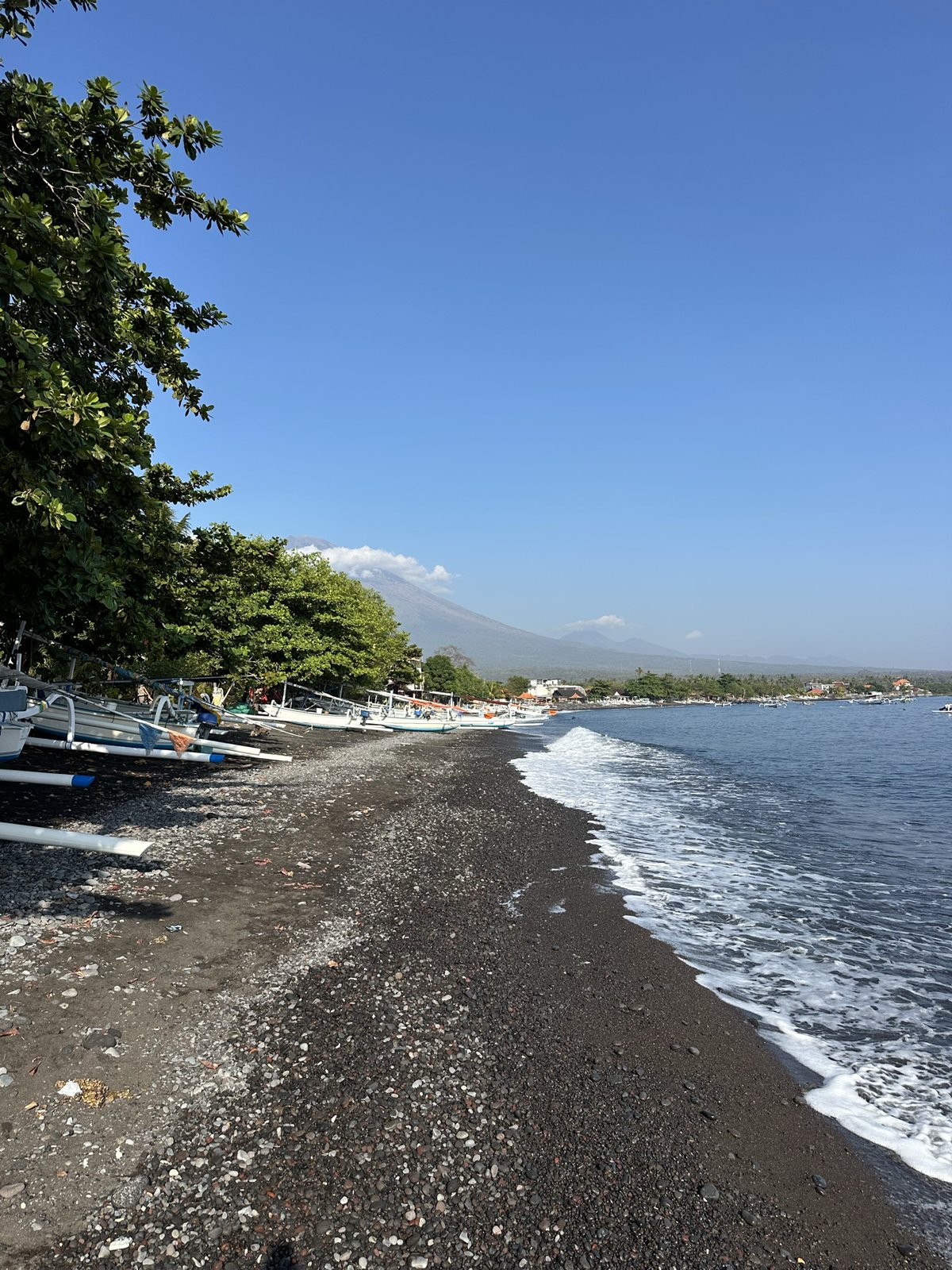 Jukungs alignés sur la plage de galets noirs d'Amed, vague au premier plan