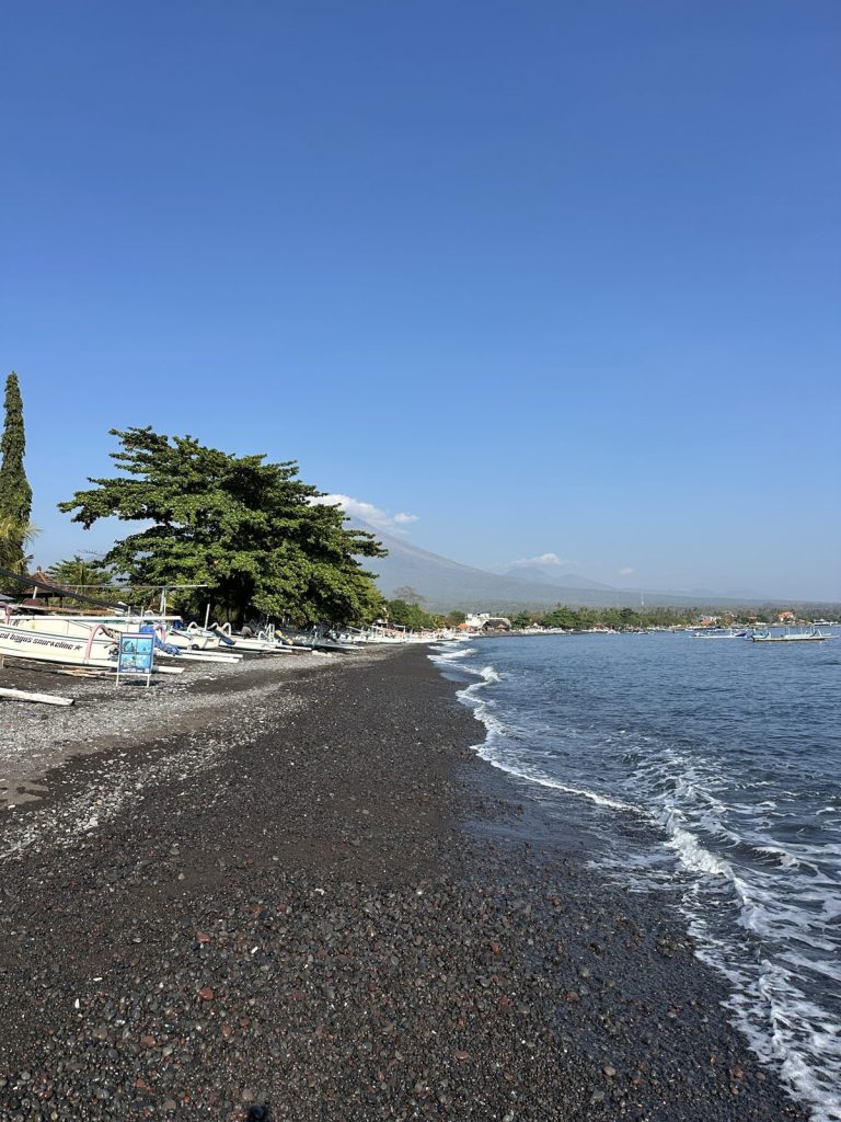 Plage de galets noirs d'Amed avec des jukungs et le Mont Agung dans les nuages