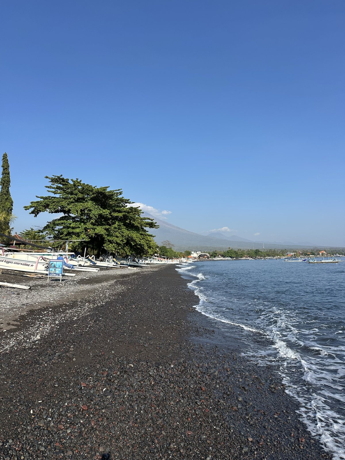 Plage de galets noirs d'Amed avec des jukungs et le Mont Agung dans les nuages