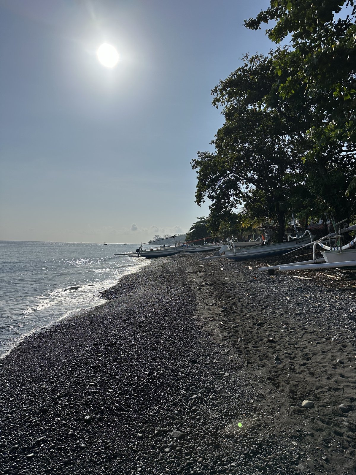 Soleil au-dessus des arbres sur la plage de galets noirs d'Amed