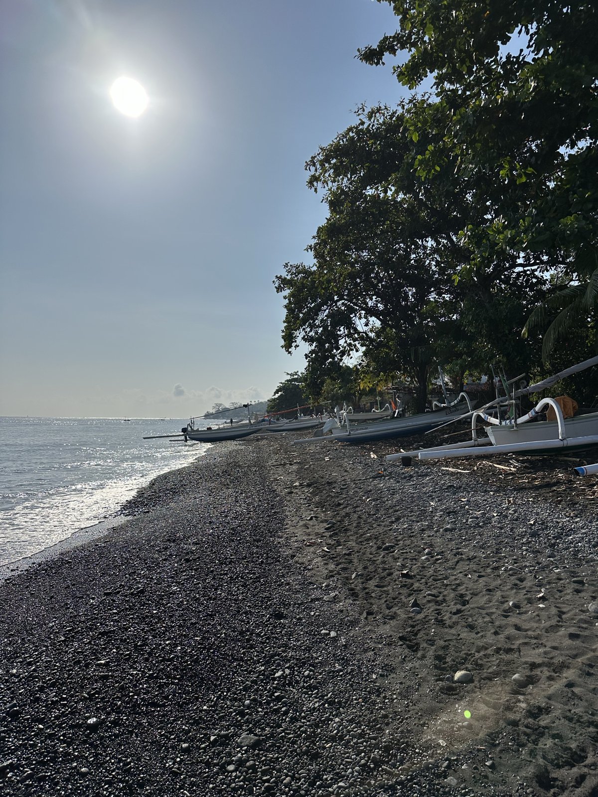 Plage de galets noirs d'Amed, soleil à travers les arbres