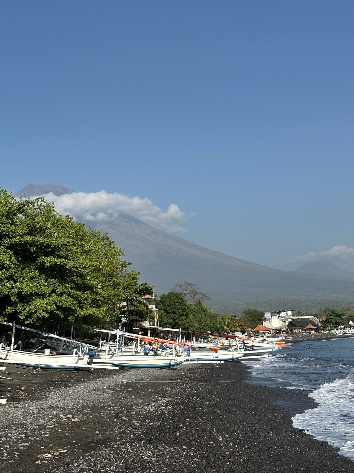Bateaux de pêche et arbres au bord de la plage d'Amed, Mont Agung nuageux